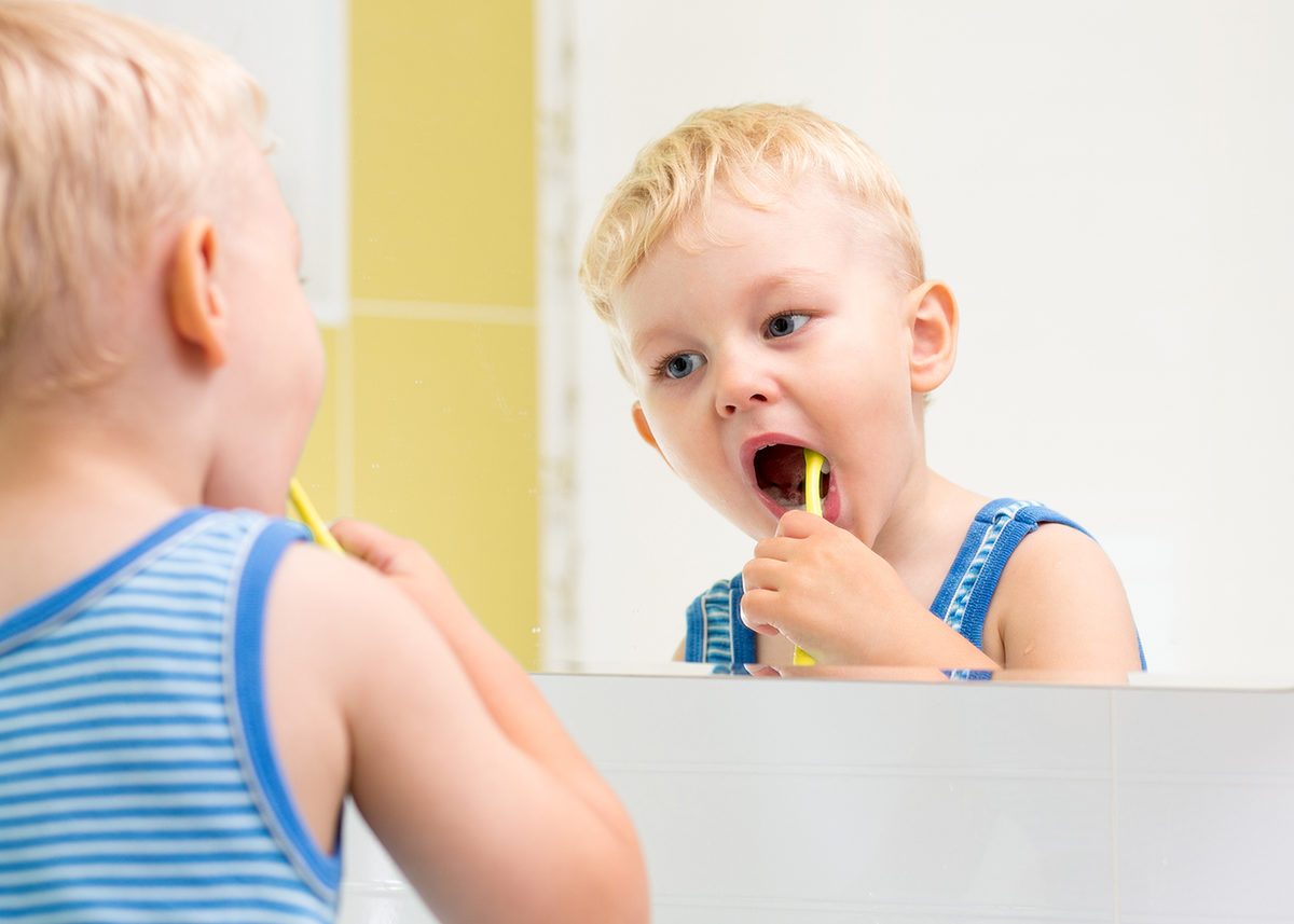 kid boy brushing teeth and looking at mirror